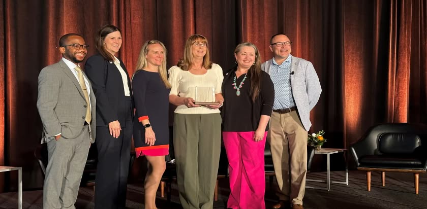 Amy Sapp holds the Patient Care Award trophy from NAPT while standing on stage with her colleagues from the UF Health Proton Therapy Institute.